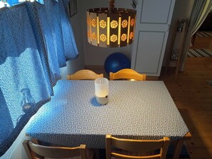 A dining area with a table covered by a patterned tablecloth, wooden chairs, and a hanging light fixture with a geometric design. - Off Grid at Fjätälven (Sarna)