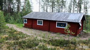 A red cabin with a metal roof, surrounded by dense forest. - Off Grid at Fjätälven (Sarna)