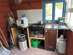 A compact kitchen with a gas stove, a sink, and a window overlooking a forested area. - Off Grid at Fjätälven (Sarna)