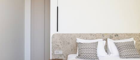 Een slaapkamer met een bed, kussens, een nachtkastje en een kledingkast.