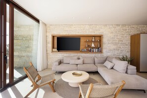 Ein modernes Wohnzimmer mit Steinwand, großem Flachbildfernseher, beigem Sofa und Korbstühlen.