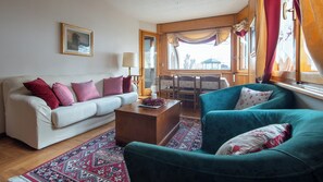 A living room with a white sofa, a teal armchair, a wooden coffee table, and a patterned rug. - Funivie 24 - Praimont (Bormio)