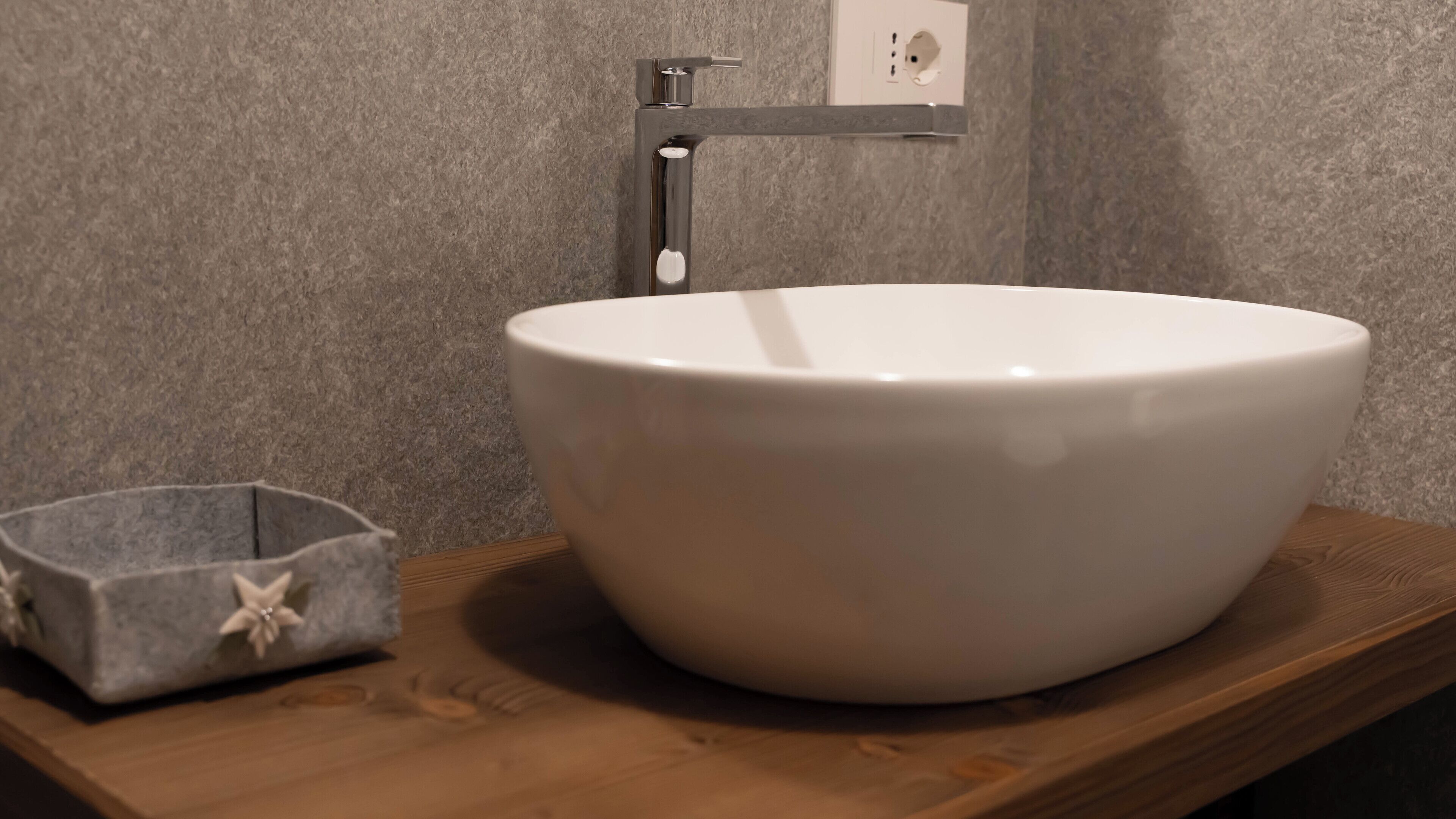 A bathroom with a white sink on a wooden countertop, a small gray container with a star design, and a wall-mounted faucet.