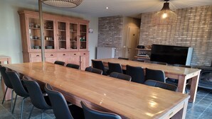 A spacious dining area with a long wooden table and black chairs, a wooden cabinet with glass doors, and a brick-patterned wall. - Countryside holiday home (Gijverinkhove)