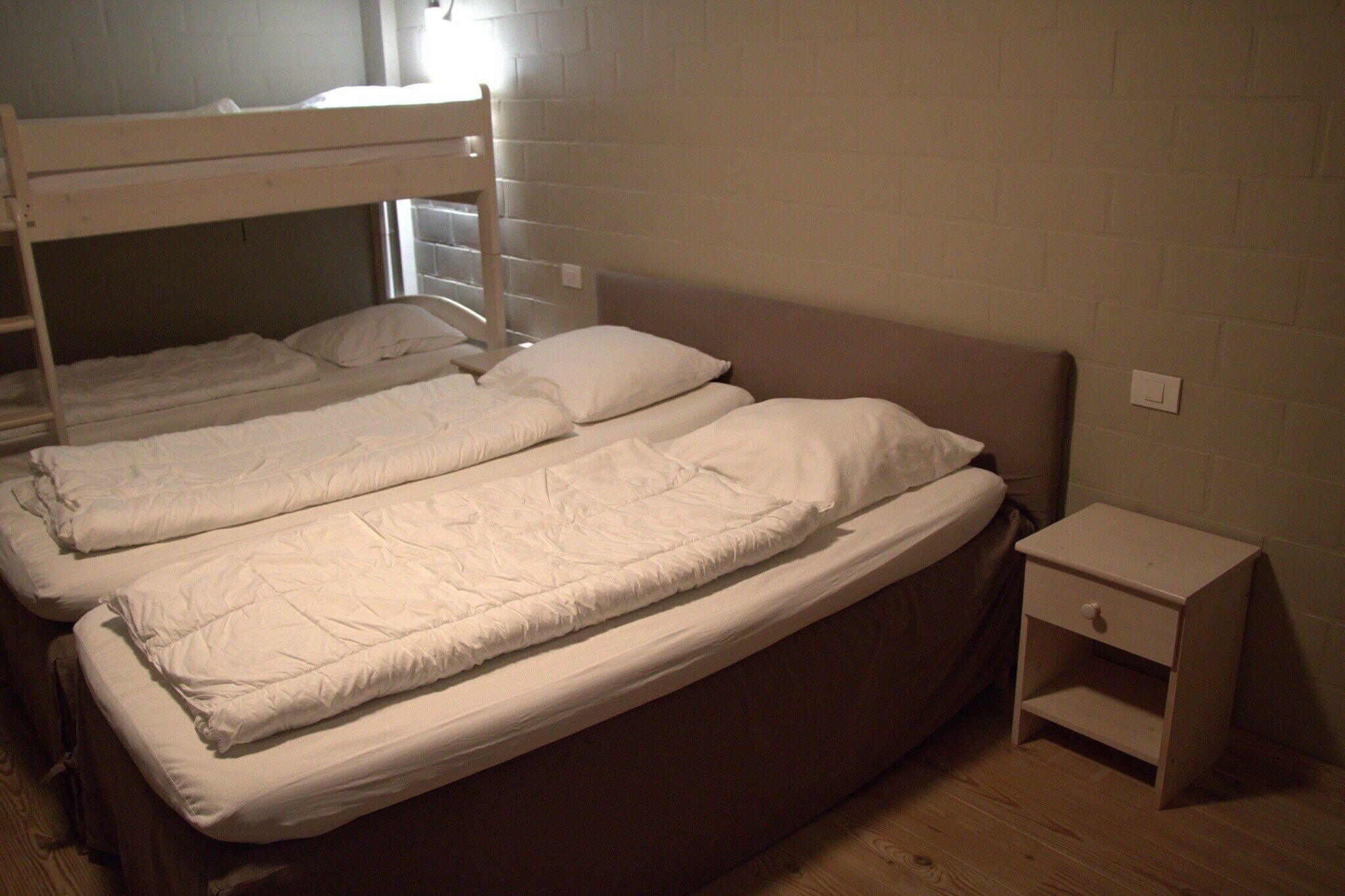 A room with two bunk beds, a bedside table, and a small shelf.