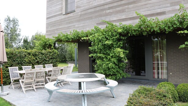 An outdoor patio with a round table and six chairs, a brick wall, and a hedge. - Countryside holiday home (Gijverinkhove)