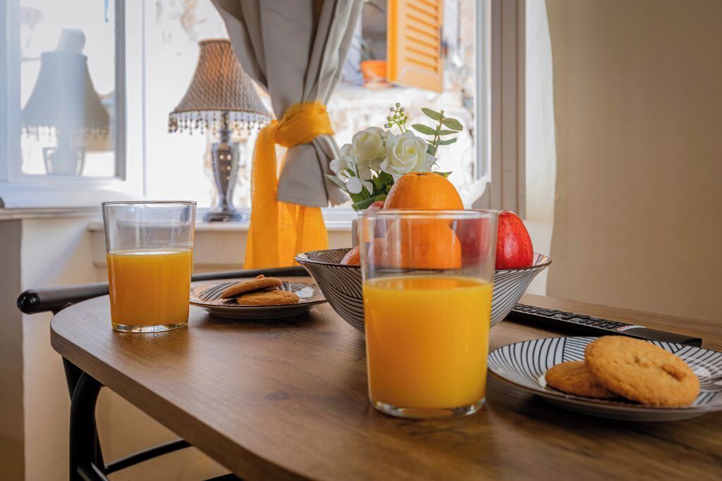 A breakfast table with orange juice glasses, a bowl of fruit, cookies, and a plate of cookies.