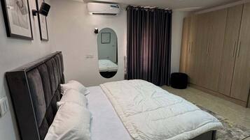Un dormitorio moderno con cama, mesita de noche, armario, espejo y equipo de aire acondicionado.