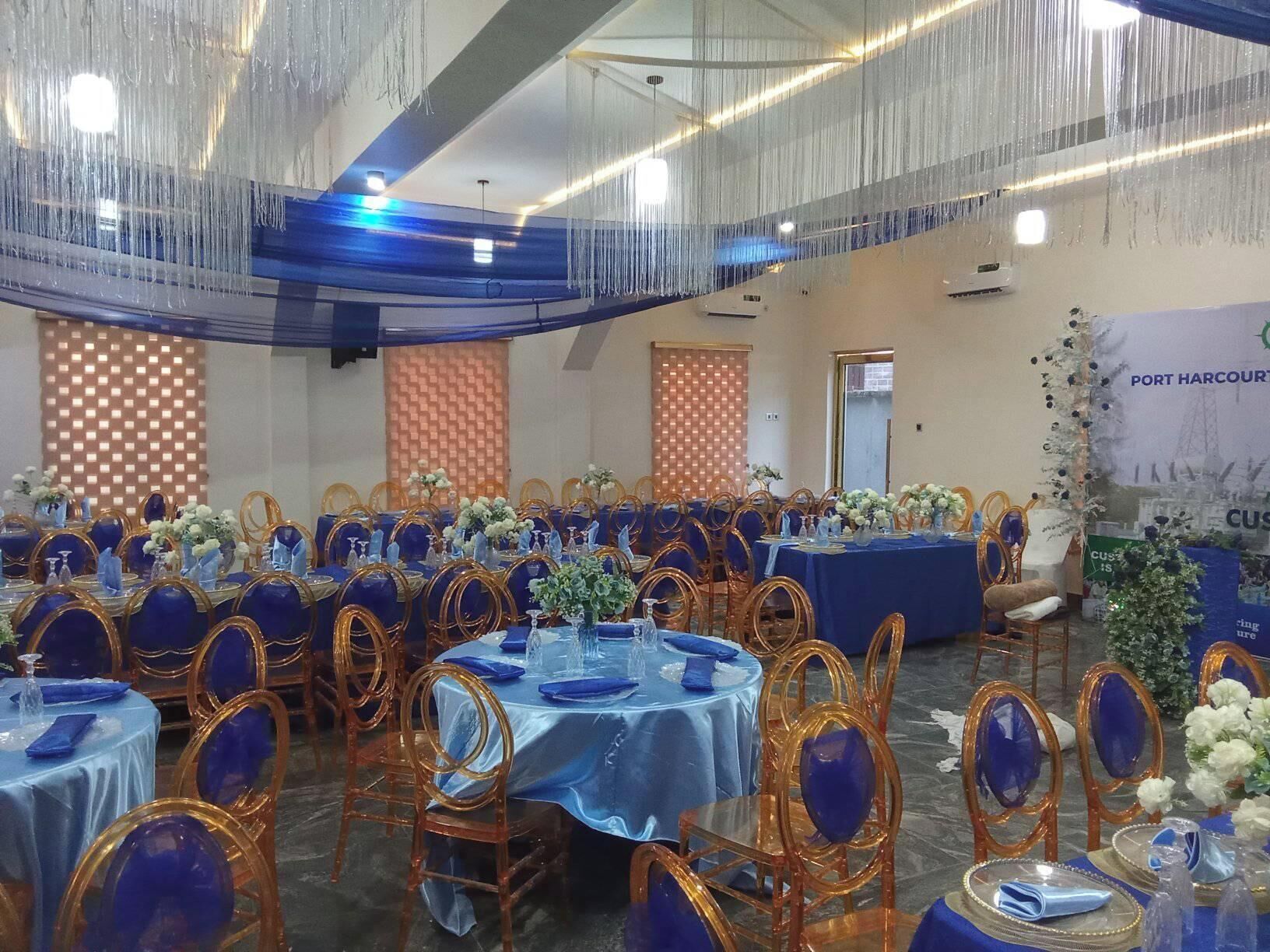 A banquet hall with round tables covered in blue tablecloths, gold chairs, and floral centerpieces.