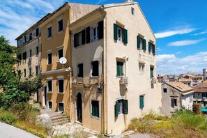 Un edificio de varios pisos con fachada color beige, contraventanas verdes y una antena parabólica.