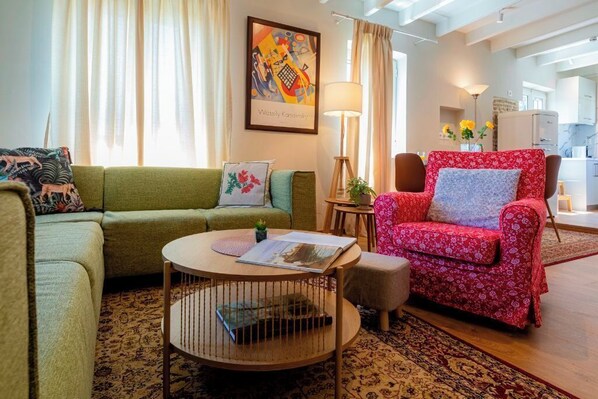 Una sala de estar acogedora con un sofá verde, un sillón rojo estampado y una mesa de centro redonda.