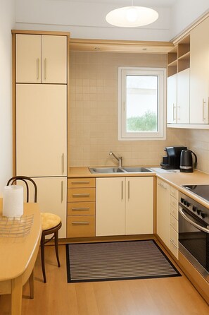 A compact kitchen with a window, a sink, a stove, and a dining area with a chair and table. - Verdant Escape Corfu (Corfu)