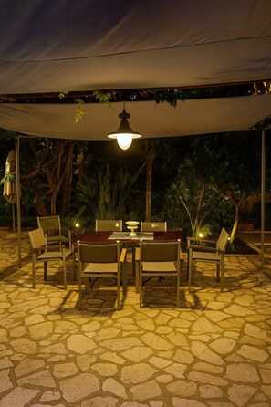 Een terras met een stenen vloertegel, een tafel met stoelen en een overkapping.