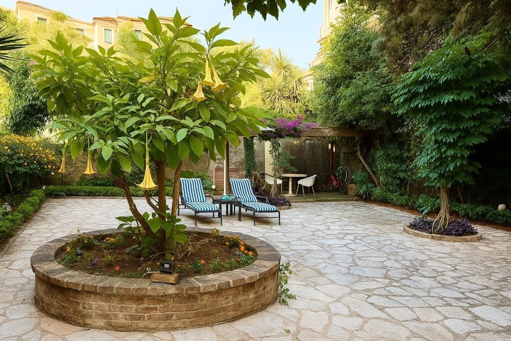 A courtyard with a stone floor, a central planter with a tree, and blue-striped chairs.