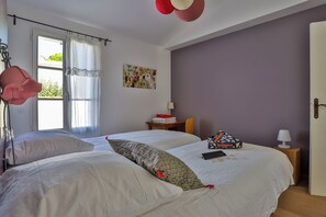 Ein Schlafzimmer mit zwei Betten, einem Fenster mit Vorhängen, einem Tisch mit Lampe und einem Bild an der Wand.