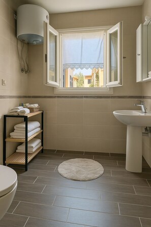 A bathroom with a window, a sink, a toilet, and shelves with towels. - Spianada Dimora Corfu (Corfu)