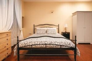 A bed with a patterned bedspread, a bedside table with a lamp, a wooden dresser, and a wardrobe. - Spianada Dimora Corfu (Corfu)