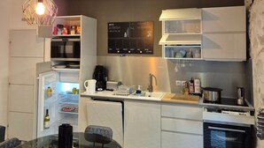 A compact kitchen with a dining area, featuring a refrigerator, microwave, stove, and a chalkboard menu. - Charming 3★ Holiday Home — Historic Heart of Béziers, Peaceful Courtyard, Secret (Béziers)