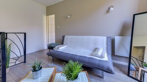 A modern living room with a grey sofa, two white cushions, and a small potted plant on a patterned rug. - Charming 3★ Holiday Home — Historic Heart of Béziers, Peaceful Courtyard, Secret (Béziers)