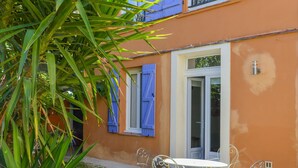 A small outdoor seating area with a table and chairs, a door with a window, and a wall with a water spigot. - Charming 3★ Holiday Home — Historic Heart of Béziers, Peaceful Courtyard, Secret (Béziers)