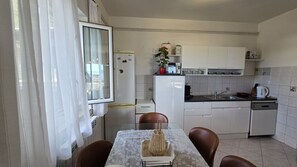 Eine kompakte Küche mit weißen Schränken, einem Kühlschrank, einer Mikrowelle und einem Spülbecken. Ein Esstisch mit Stühlen und eine Vase mit Blumen sind ebenfalls vorhanden.