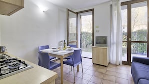 Una cocina compacta con estufa a gas, una mesa de comedor con sillas, un televisor y un sofá.