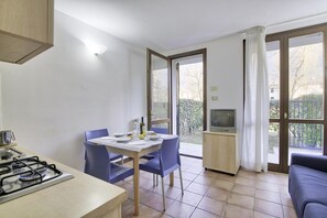 A compact kitchen with a gas stove, a dining table with chairs, a television, and a sofa. - Mobilehome am Luganersee (Porlezza)