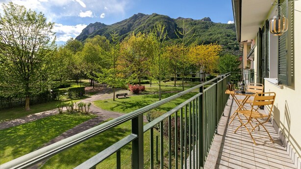Un balcón con vistas a la montaña, un jardín con árboles y una mesa con sillas.