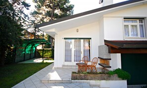 A modern house with a patio, two wicker chairs, and a green garden. - Cozy Villa With Patio and Garden (Lignano Sabbiadoro)