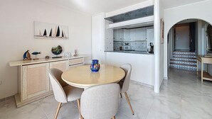 A dining area with a round table and chairs, a kitchen with white cabinets, and a view of a staircase. - BELLA PANORAMICA Roses / Roses - INTERimmo (Rosas / Roses)