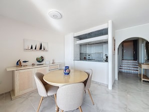 A dining area with a round table and chairs, a kitchen with white cabinets, and a view of a staircase. - BELLA PANORAMICA Roses / Roses - INTERimmo (Rosas / Roses)