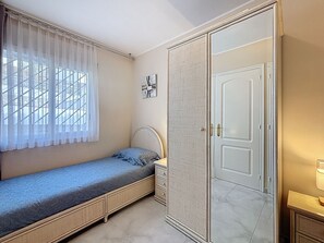 A bedroom with a single bed, a wardrobe, a small bedside table, and a window with sheer curtains. - BELLA PANORAMICA Roses / Roses - INTERimmo (Rosas / Roses)