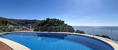 A swimming pool with a clear view of the sea and hills in the background.