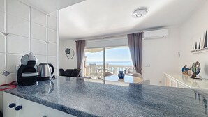 A modern kitchen with a granite countertop, a coffee maker, and a view of the sea through the balcony. - BELLA PANORAMICA Roses / Roses - INTERimmo (Rosas / Roses)