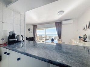 A modern kitchen with a granite countertop, a coffee maker, and a view of the sea through the balcony. - BELLA PANORAMICA Roses / Roses - INTERimmo (Rosas / Roses)