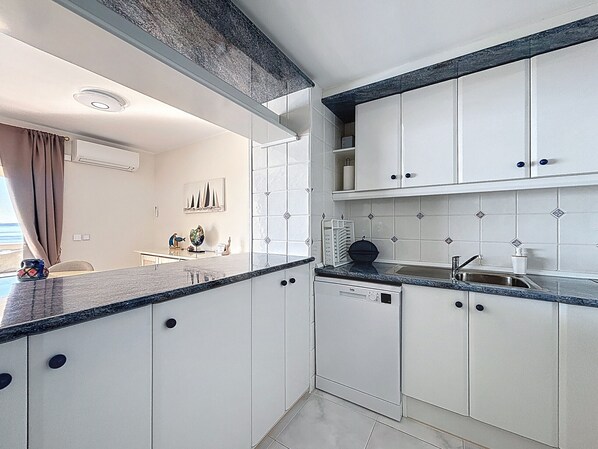 A modern kitchen with white cabinets, a granite countertop, and a built-in dishwasher. - BELLA PANORAMICA Roses / Roses - INTERimmo (Rosas / Roses)