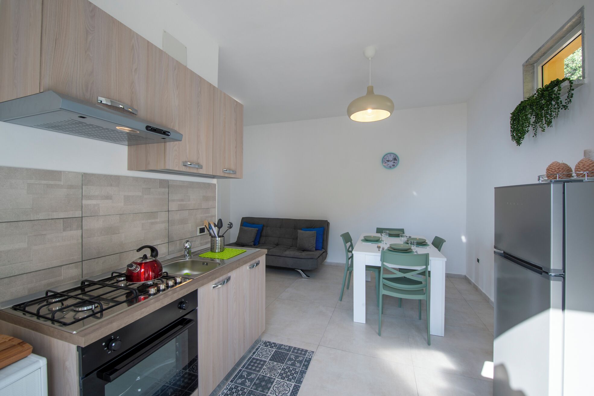 Une cuisine moderne équipée d’une cuisinière à gaz, d’un four et d’un réfrigérateur encastré. On y trouve un coin repas avec une table et des chaises, ainsi qu’un canapé à l’arrière-plan.