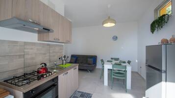 Une cuisine moderne équipée d’une cuisinière à gaz, d’un four et d’un réfrigérateur encastré. On y trouve un coin repas avec une table et des chaises, ainsi qu’un canapé à l’arrière-plan.