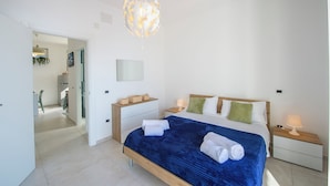 A modern bedroom with a large bed, bedside tables, a hanging light fixture, and a view into the adjacent room. - VivimiHome - Casa Angelina (Conca dei Marini)