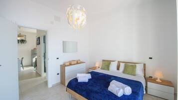Une chambre moderne avec un grand lit, des tables de chevet, un luminaire suspendu et une vue sur la pièce adjacente.