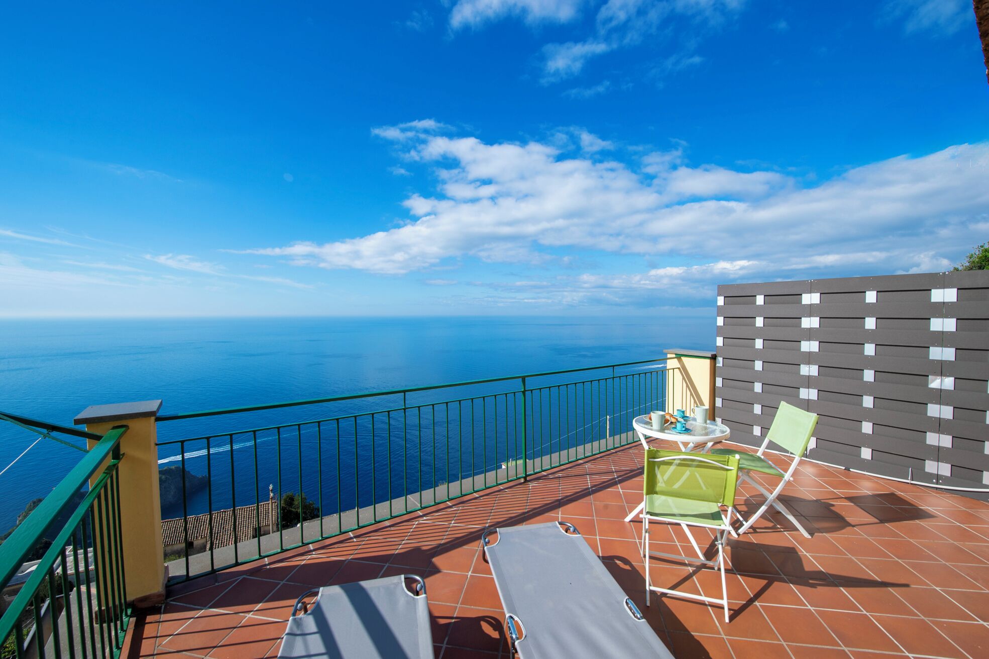 A balcony with a view of the sea, a table with chairs, and a tiled floor.