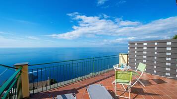 A balcony with a view of the sea, a table with chairs, and a tiled floor.