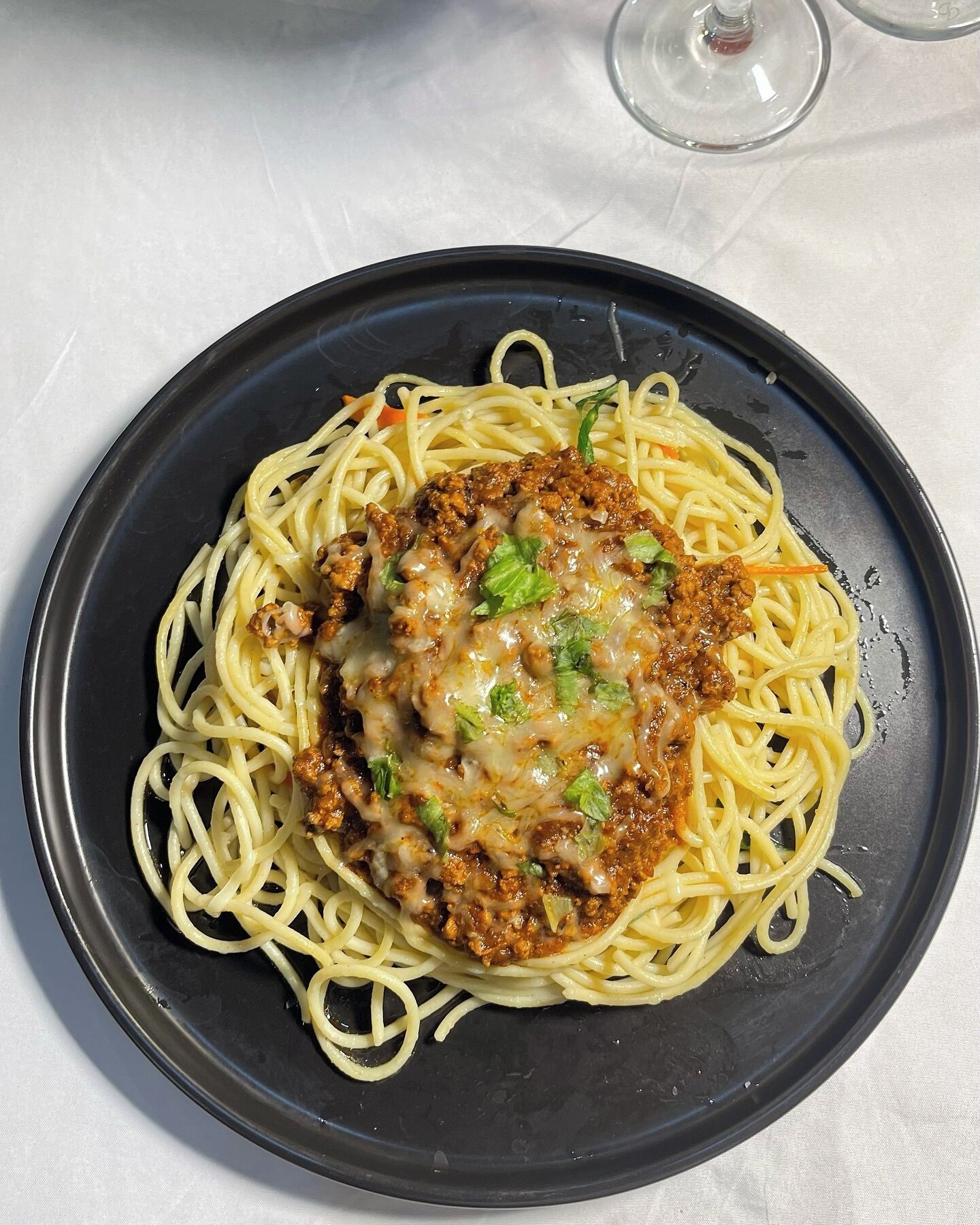 A plate of spaghetti with a meat-based topping and melted cheese, served on a dark plate.