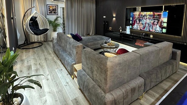 Ein modernes Wohnzimmer mit einem Ecksofa, einem Hängekorbstuhl, einem Flachbildfernseher und einem Deckenventilator.