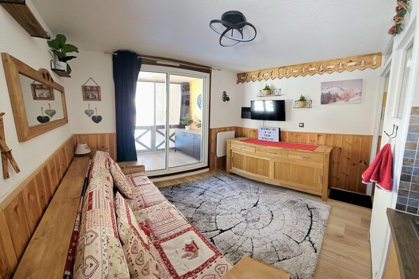 A room with a wooden bench, a television, a wooden cabinet, and a large window. - Ski Base for 4 near La Foux Lifts (Allos)