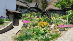 Un village européen traditionnel, avec des bâtiments en pierre, un chemin pavé et une variété de fleurs aux couleurs vives dans le jardin.