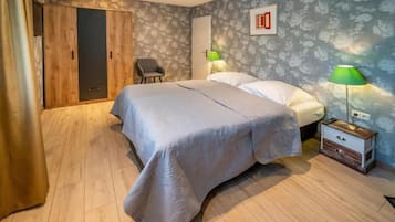 Een slaapkamer met een bed, een stoel, een garderobe en een nachtkastje met een lamp.