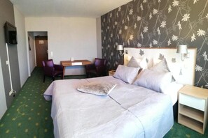 Hotelkamer met een bed, een bureau, twee stoelen, een televisie en een bloemenpatroon op de muur.