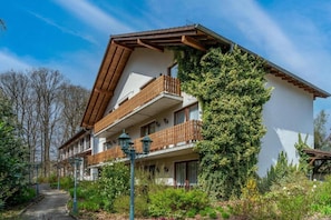 A multi-story building with balconies, a pathway, and surrounding greenery.
