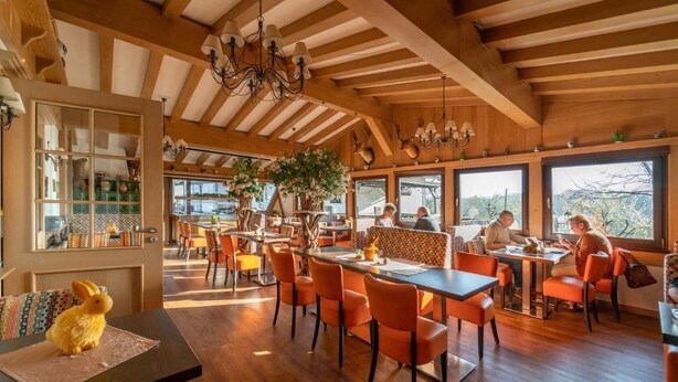 Un restaurant avec des poutres en bois, des chaises orange et de grandes fenêtres.